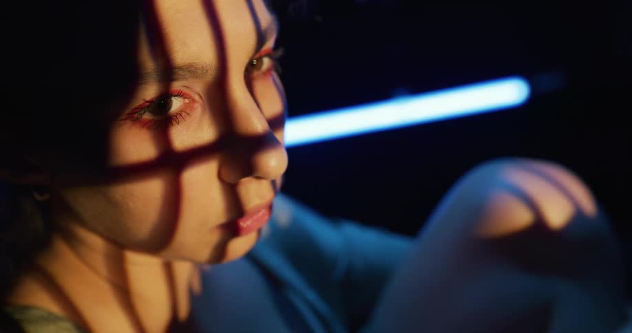 Close up of shadows on the face of a young woman sitting inside a dimly lit room
