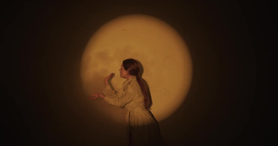 Woman dances in front of wall under a soft spotlight while smoke rises