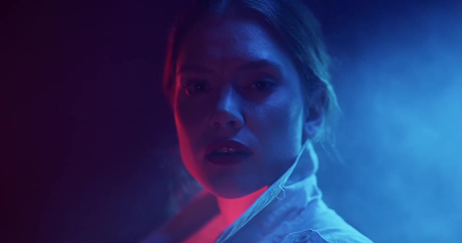 A woman is standing outside in the darkness as light illuminates smoke rising behind her