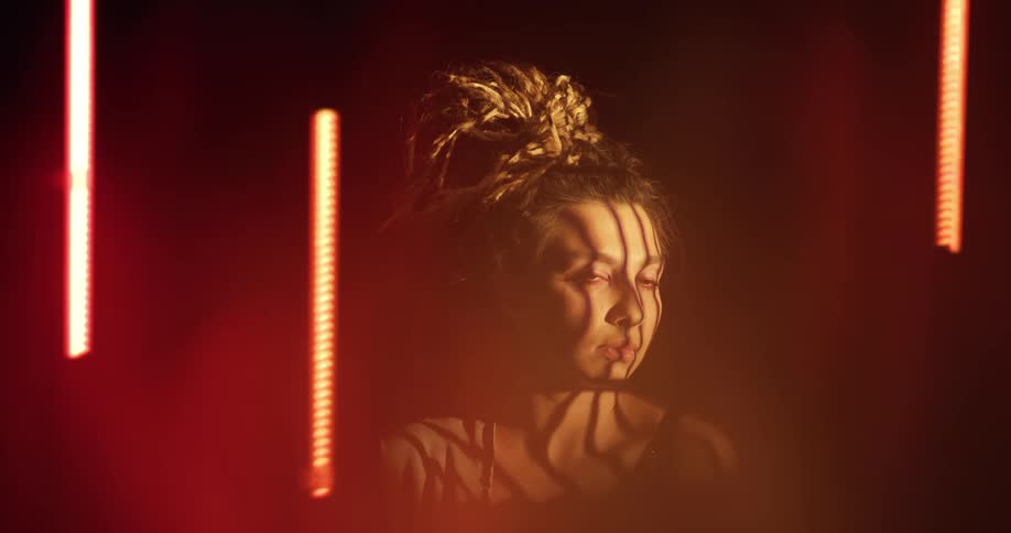 Bars of light and shadow on a womans face from odd glowing tubes of light