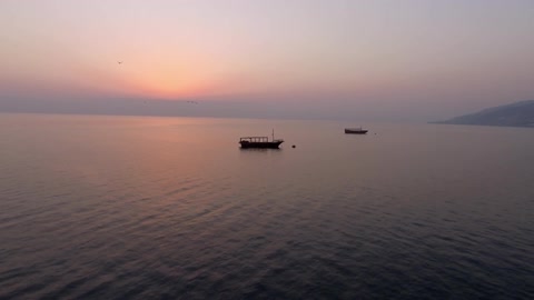 Two boats are in the water as birds fly overhead