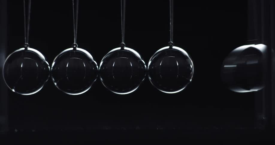 Metal balls are swinging back and forth in the darkness hitting each other in a newtons cradle