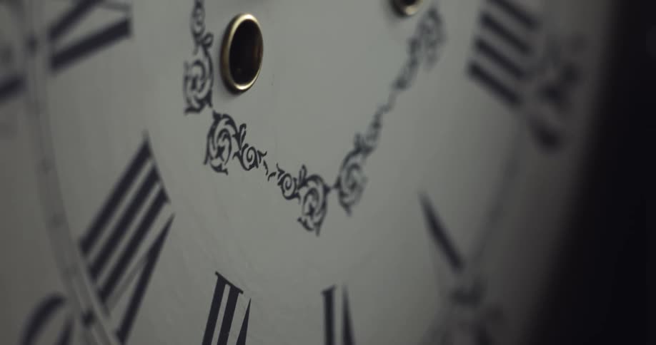 The hands of an analog clock cast a shadow on the clock face near the roman numerals