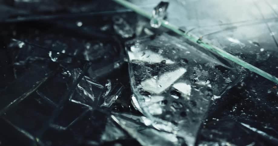 Pieces of broken glass sprinkled with water on the ground of a dark room reflecting light