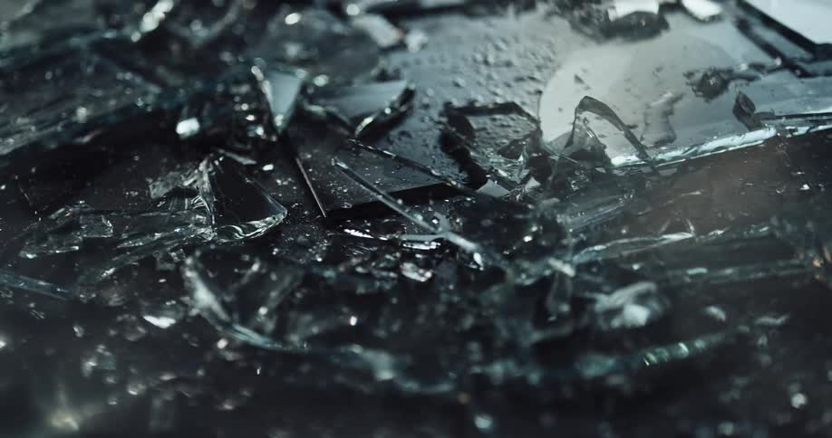 Pieces of broken glass sprinkled with water on the ground of a dark room reflecting light