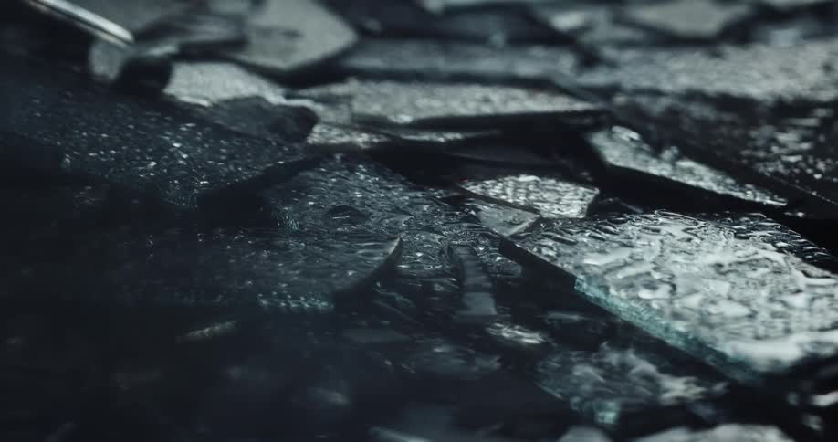 Close up of rain falling over pieces of broken glass on the ground close to red and blue flashing lights