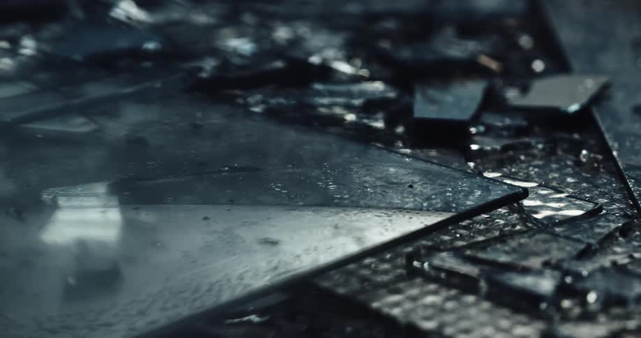 Pieces of broken glass sprinkled with water on the ground of a dark room reflecting red flashing lights