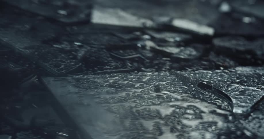 Pieces of broken glass sprinkled with water on the ground of a dark room reflecting light