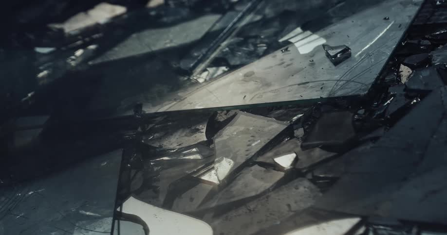 Pieces of broken glass sprinkled with water on the ground of a dark room reflecting light