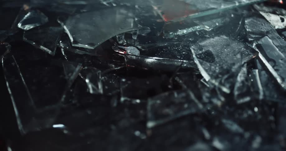 Pieces of broken glass sprinkled with blood stains on the ground of a dark room reflecting light