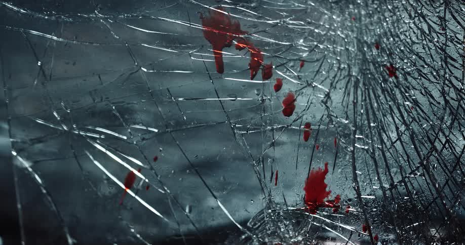 Blood is splattered on shattered glass as red lights flash upon it