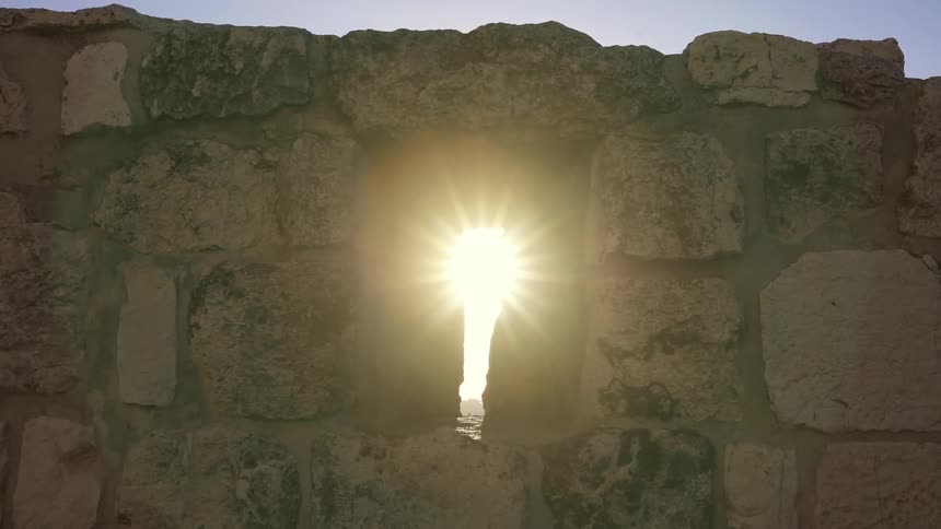 The sun beams through an opening in an ancient stone wall