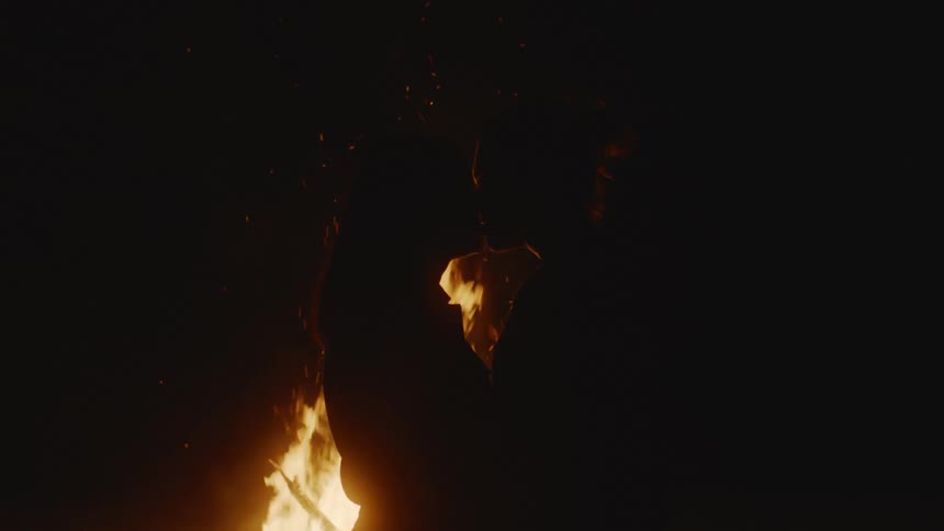 Silhouette of a young couple kissing in front of a large bonfire at night