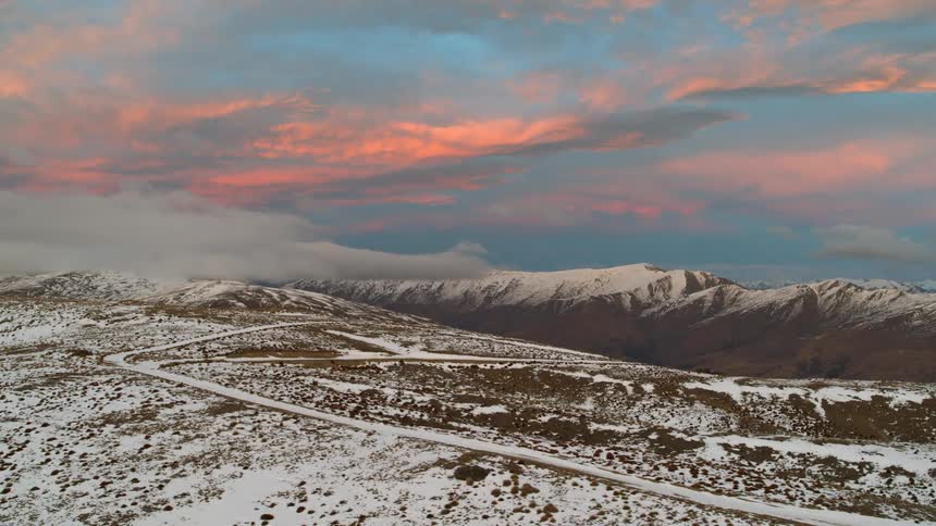 Aerial view of a road running up the gentle slopes of a mountain covered in snow at sunset