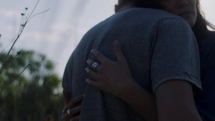 Woman hugging his boyfriend and running her hand through his back while theyre standing outdoors at nature