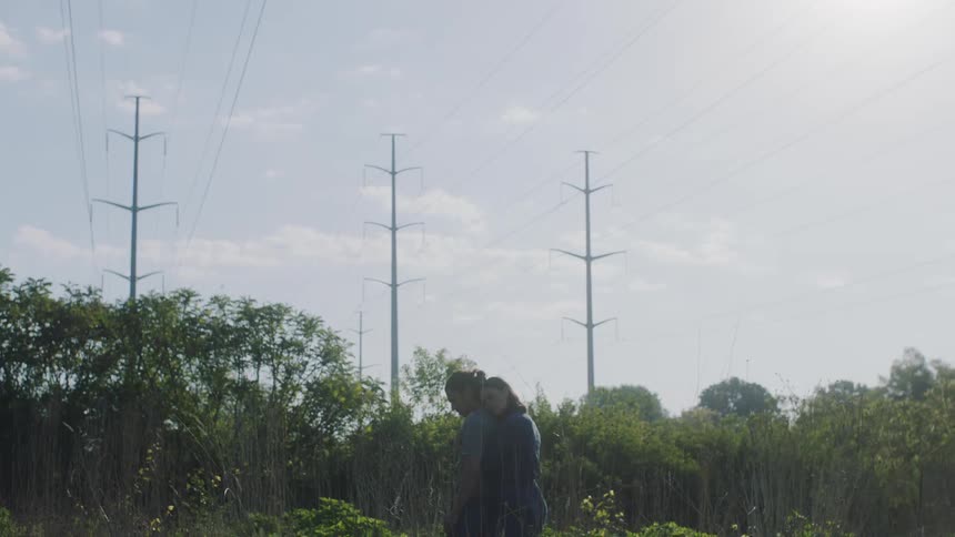 A woman in a garden stands behind a man and hugs him