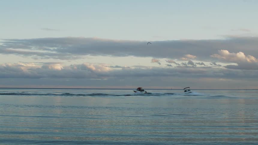 Two boats are traveling in a circle on a lake on a cloudy evening