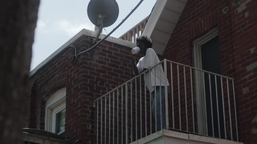 Woman stands on balcony drinking coffee while leaning against the rail
