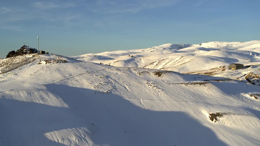 Shadows lie on side of snow covered hill topped with a pole that overlooks buildings