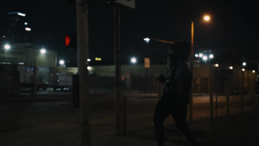 A young man wearing a hoodie runs on a city street taking a sharp corner at night