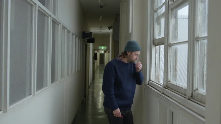 A man coughs while standing in the hallway at a hospital