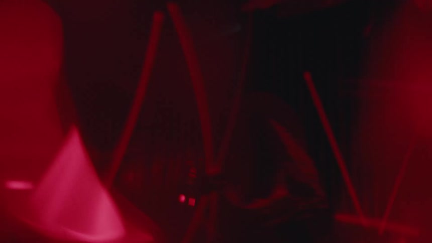 A person in a mask moves among laser lights in the darkness