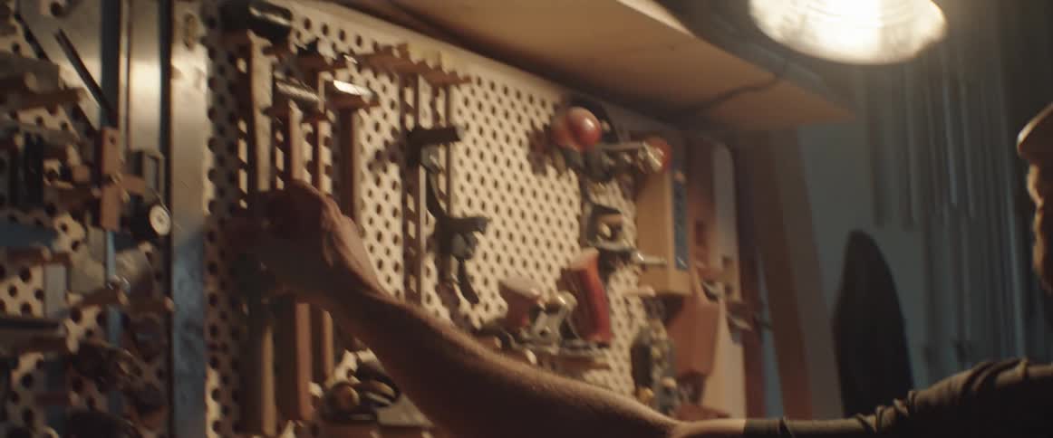 A man grabs a hammer from a wall of tools in his work shop