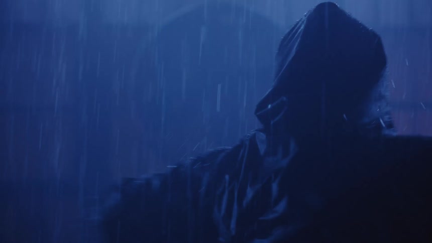 A man wearing a hood and a glowing x eyes face mask spins and dances in the rain