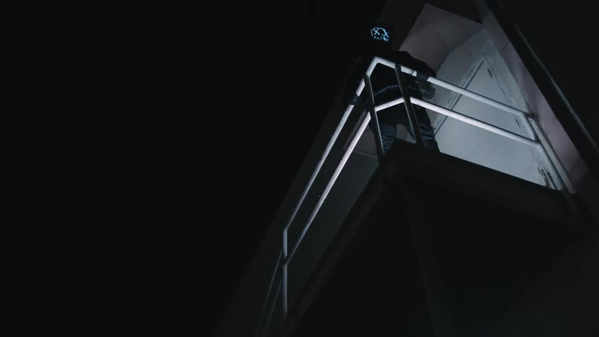 A masked person holds onto a railing while overlooking a factory floor