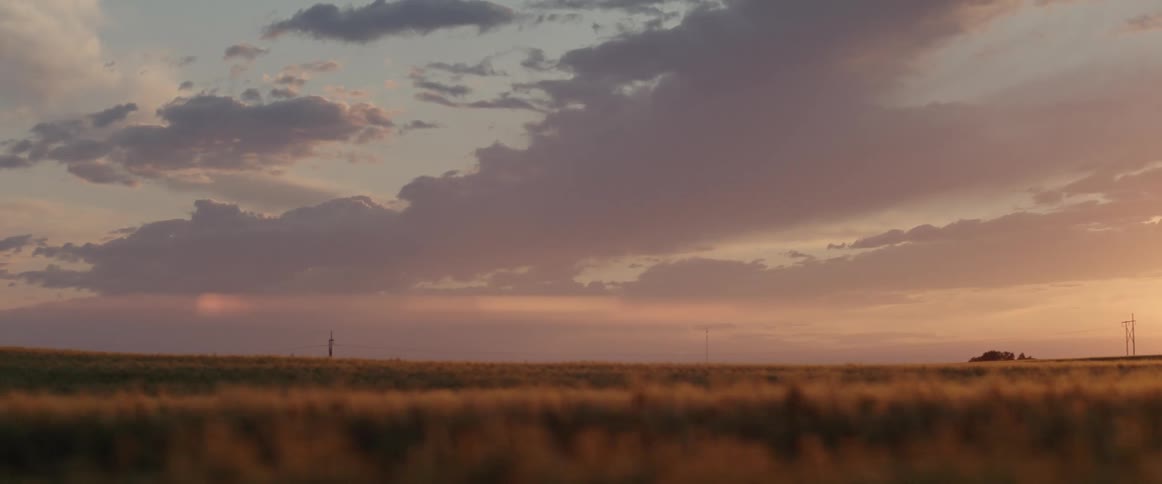 The sun is setting over a large grassland with red clouds