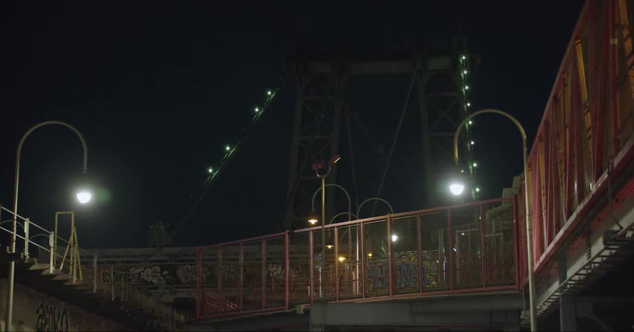 Light shines in the darkness as a cyclist rides across a downtown foot bridge among graffiti painted walls with a headlight on