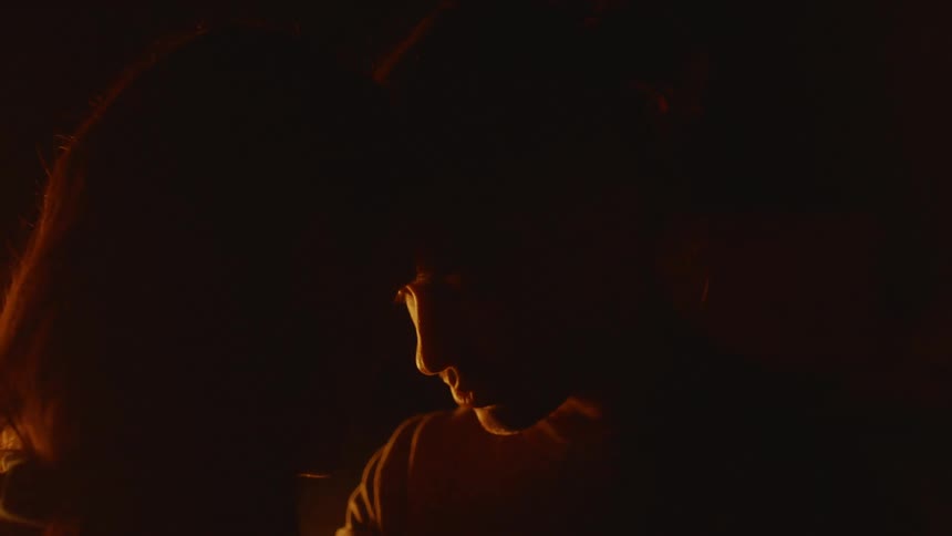 Young couple standing by a campfire at night gently touching heads against each other