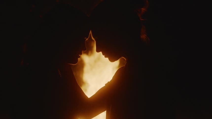 Young couple standing in front of a campfire touching heads and romantically looking into each other eyes