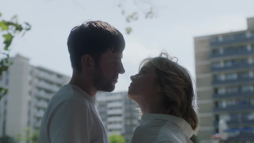A man and a woman are standing outside very close to each other lovingly staring into each others eyes while the camera spins around them