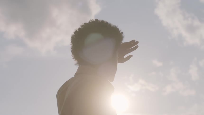Young black man standing outdoors covering his face from the sunlight with his hand