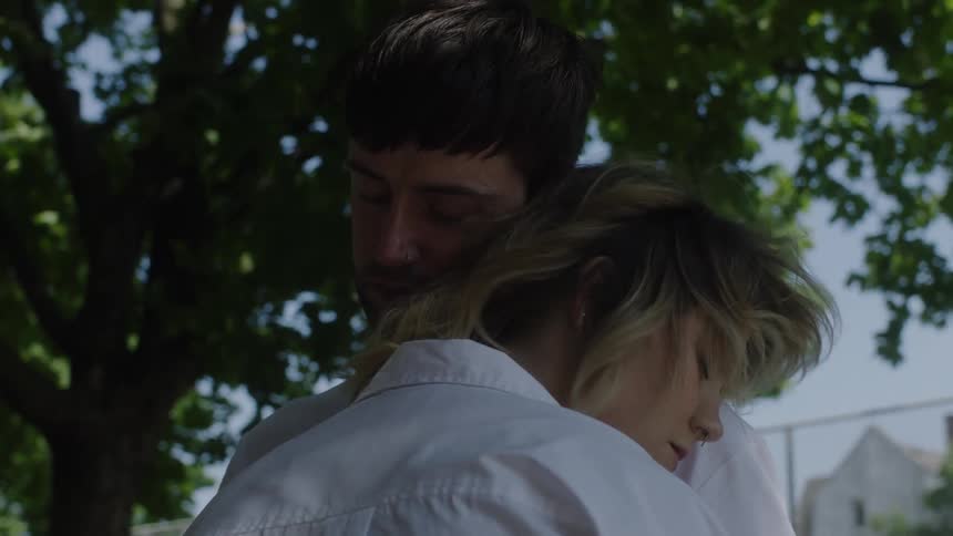 A man and woman embrace tightly outside with wind blowing through the womans hair
