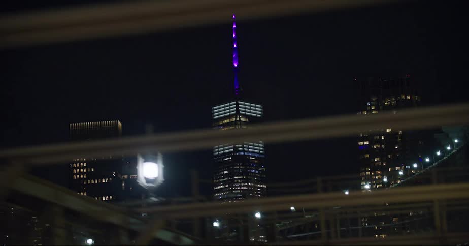 Illumianted skyscraper with purple spire and high rise buildings at night in the city