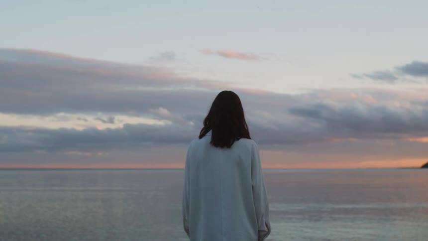 A woman looks out towards the ocean at sunset