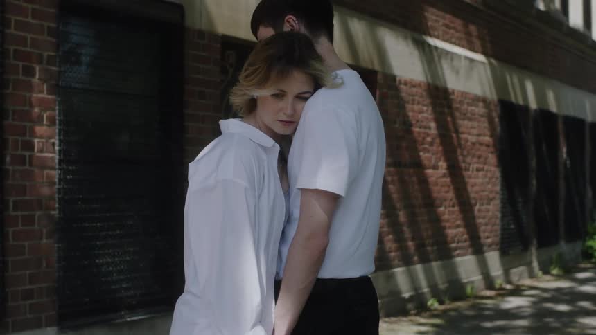A couple embrace on a sidewalk outside a building