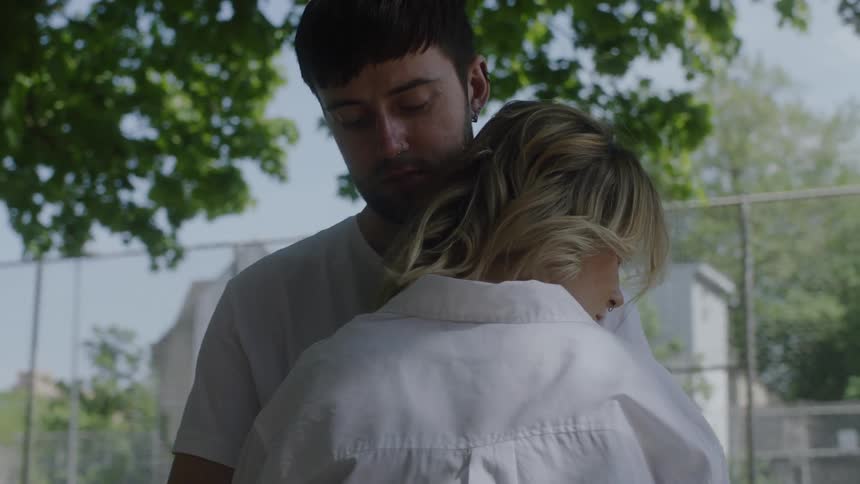 Young couple standing outdoors at a public area in the city hugging each other with thoughtful and sad expressions in the face