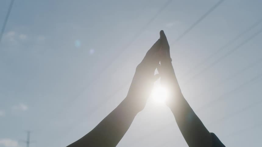 Two people with their arms up gently touching each others hands outdoors at a sunny day