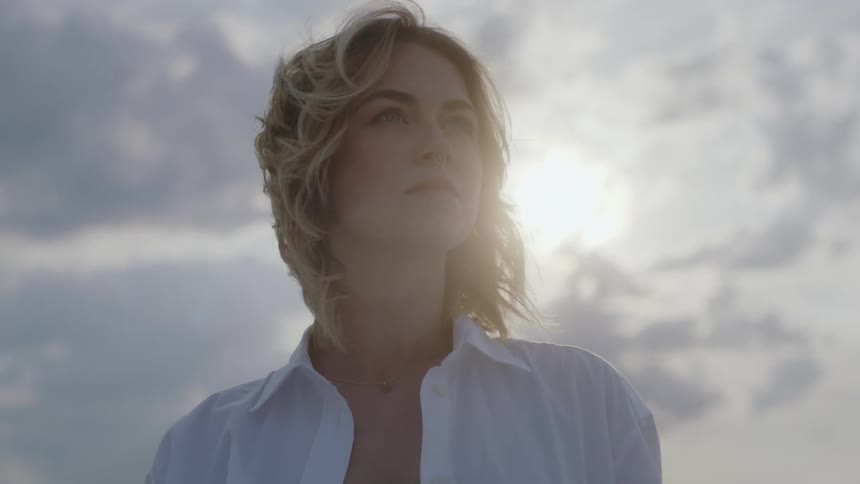 Blonde woman standing outdoors looking ahead during a cloudy day