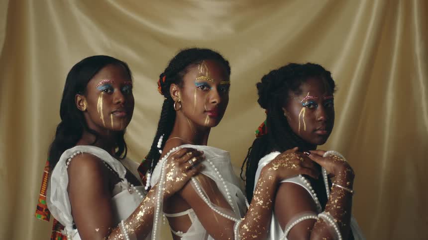 Three young women in costume and gold colored body paint makeup stand posed together