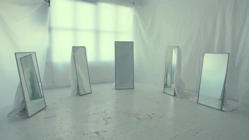 Five floor mirrors sit in a semi circle in a tarped off room