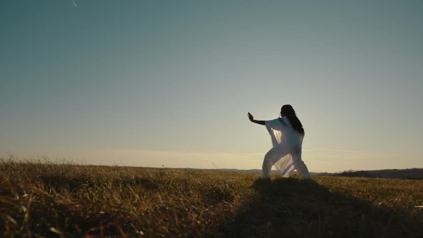 Woman wearing white clothes practices karate on a field at sunset