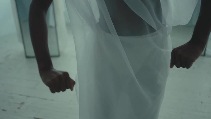 A female dancer wearing a sheer white costume dances in front of full length mirrors