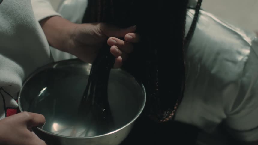 A woman dips a persons hair in a bowl of water