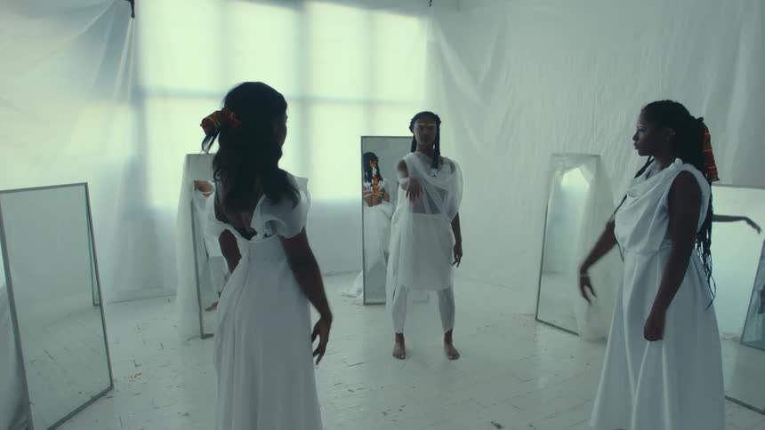 Female dancers flow through poses standing among mirrors in room with white fabric draped over walls and windows