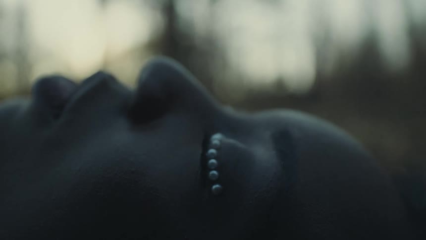 A woman lays still with her eyes closed and decorated with small beads