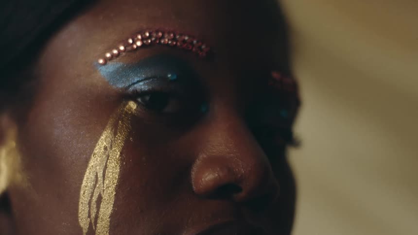 A woman poses with elaborate make up including gold streaming down her cheek like tears